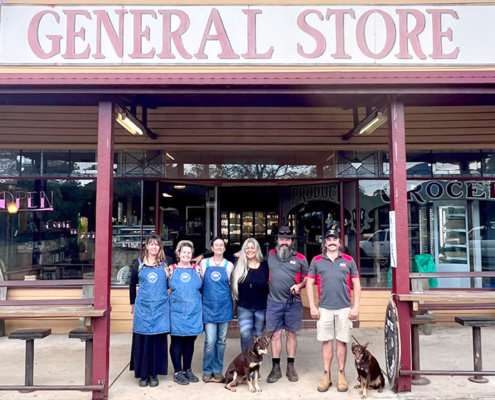 Team members standing outside Tyalgum General Store with two dogs in front of the entrance.