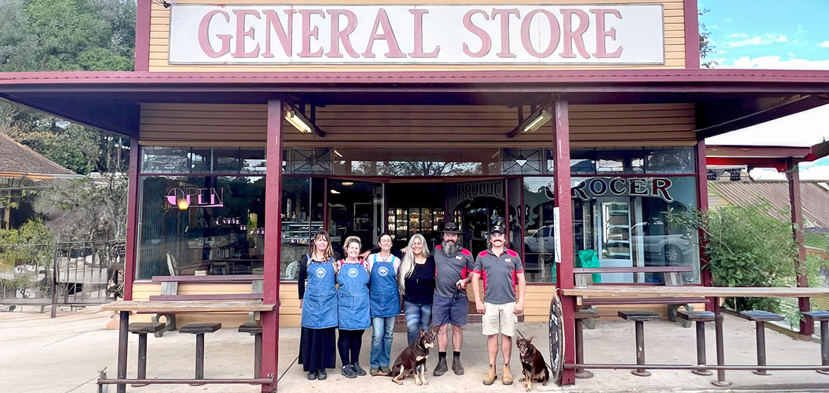 Team members standing outside Tyalgum General Store with two dogs in front of the entrance.