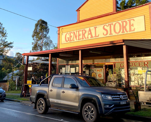 Tyalgum General Store with cars parked in front, set against a scenic backdrop of trees.