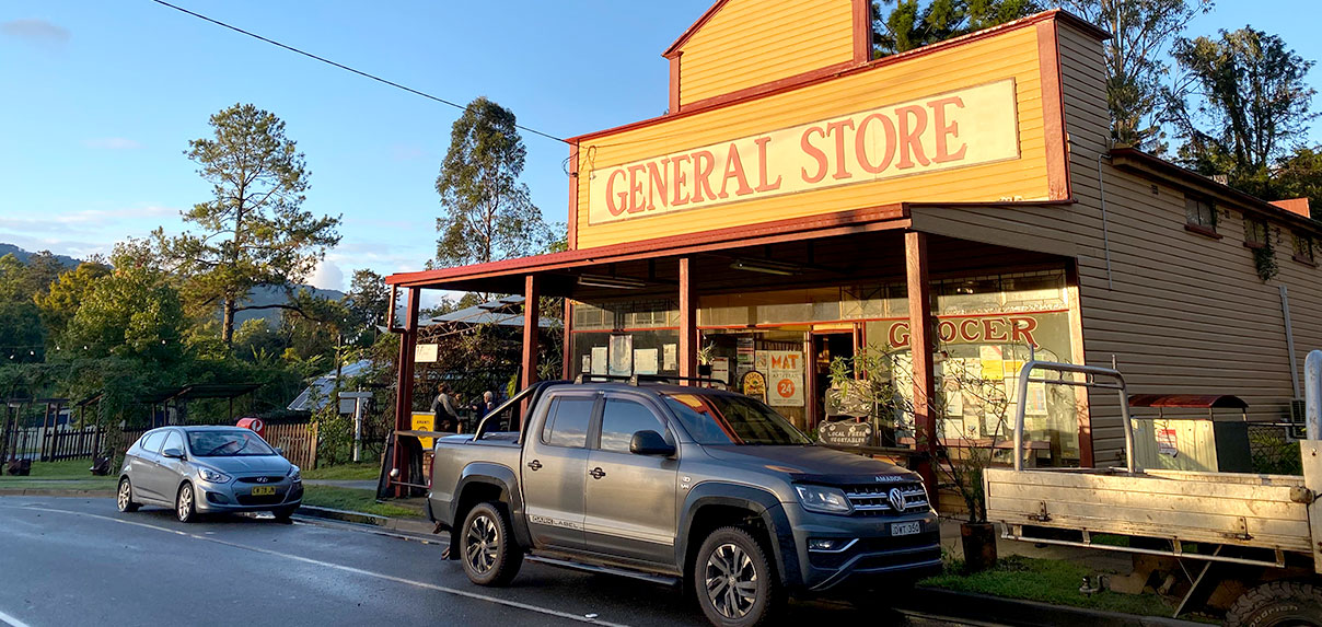 Tyalgum General Store with cars parked in front, set against a scenic backdrop of trees.