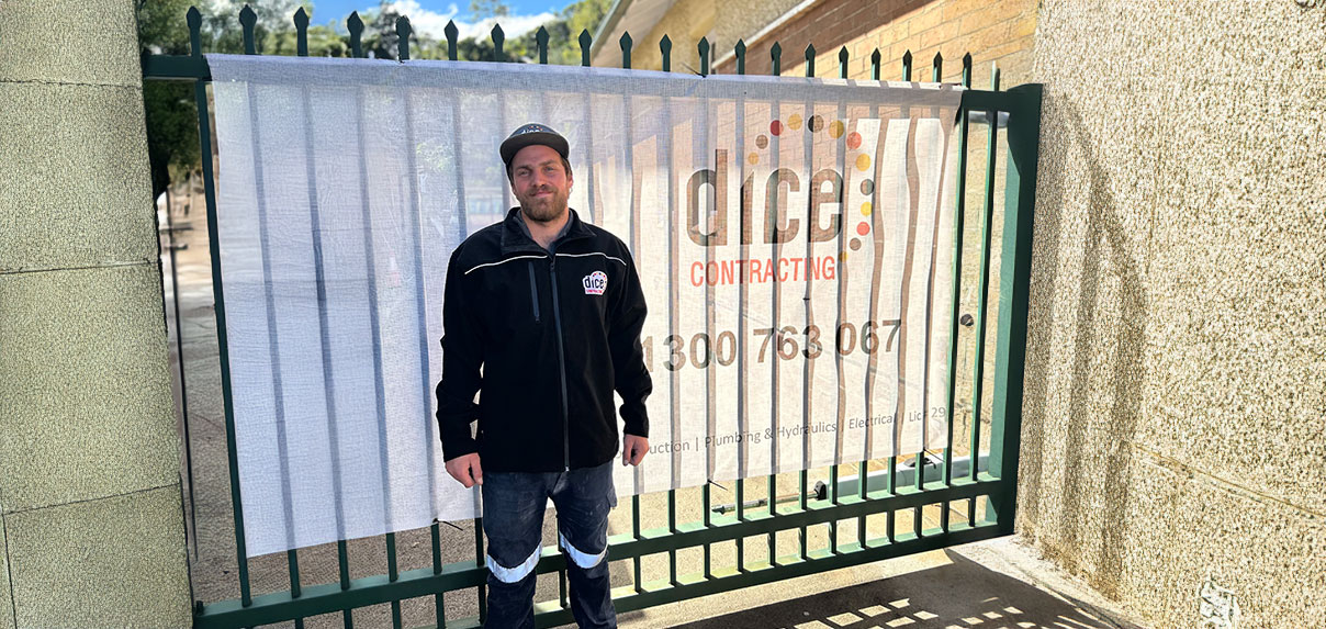 Dice Contracting worker standing in front of a fence with company banner displaying contact details.